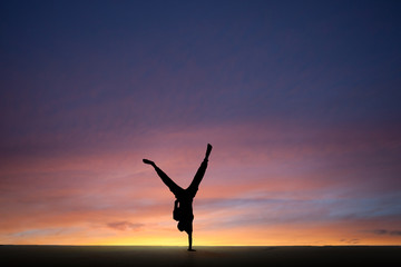 silhouetted gymnast dong one-handed handstand in sunset