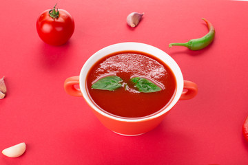Bowl of tomato soup on a red background.