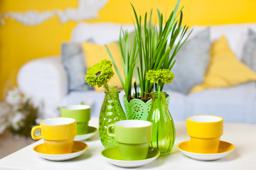 yellow and light green cups and vases with flowers and grass