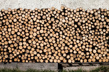 Dry firewood logs stacked up in a pile next to the house wall