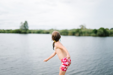 Naklejka premium Little girl throwing stones in water at the beach