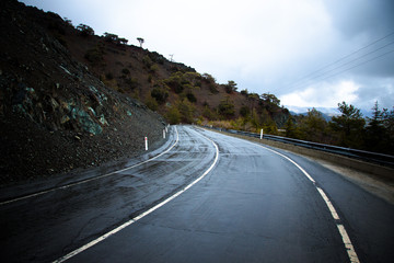 Asphalt road in the mountains. Winter. Rain. Toned