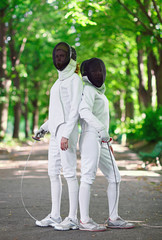 Two rapier fencers women staying in park alley getting ready for