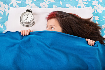 Young girl in bed hiding beneath her blanket from the alarm cloc