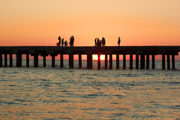 People on the old sea pier during sunset