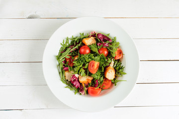 White plate with salad with rucola, tomato and chicken