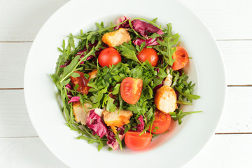 Rucola salad, tomato and chicken with parsley on white plate