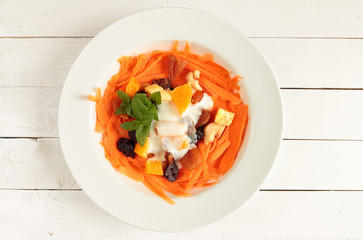 White plate with carrot, dried fruits and natural yogurt