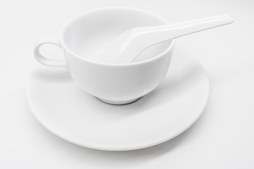 A white ceramic cup with saucer and soup spoon