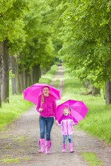 mother and her daughter with umbrellas in spring alley