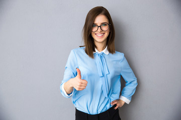Smiling businesswoman with thumb up over gray background