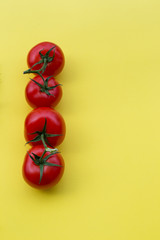 line of four tomatoes on yellow background, copy space, vertical