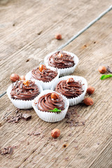 Five chocolate cupcakes with hazelnuts on top. Wooden background