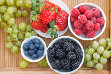 fresh berries in bowl and green grapes on wooden tray, top view
