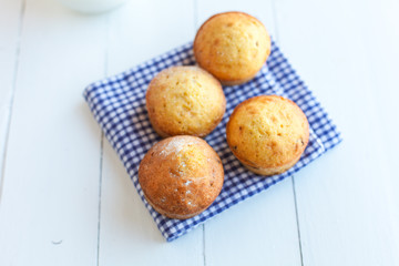 Homemade muffins in blue napkin and jug of milk on wood table. S