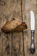 Roast beef with silver knife on wooden background.
