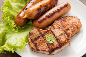 Grilled meat, sausages and vegetables on dish close up.