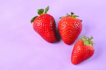 drei rote frische erdbeeren auf lila hintergrund