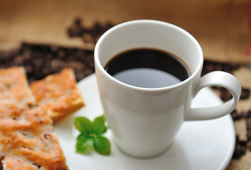 Cup of coffee and tasty cookie with coffee leaf
