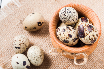 Obraz premium raw quail eggs in a wooden bowl on burlap background