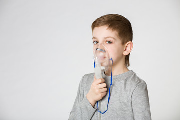 Boy breathing through inhalator mask on grey background