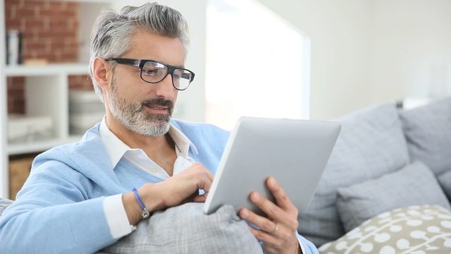 Mature man with eyeglasses websurfing on tablet at home