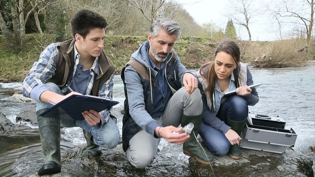 Biologist with students in science testing river water