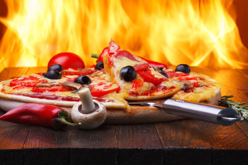 Obrazy na Szkle  Pizza na drewnianym stole z prawdziwym ogniem piekarnika na tle
