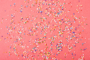 Colorful round sprinkles spilled on red background, isolated