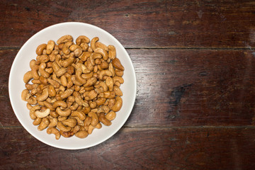 Cashew nuts in white bowl on brown wooden table, top view.