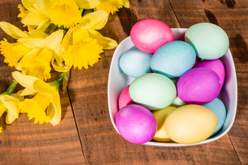 Fototapeta na wymiar Bowl of dyed Easter eggs with daffodils