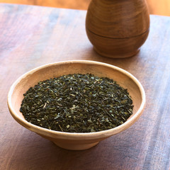 Dried green tea leaves in bowl with tea in wooden cup