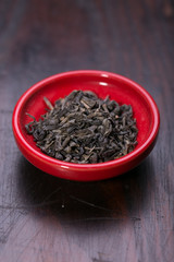 Bowl of dried green tea leaves on wooden background