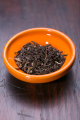 Bowl of dried green tea leaves on wooden background