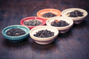 assortment of dry tea in small bowl, on wooden background