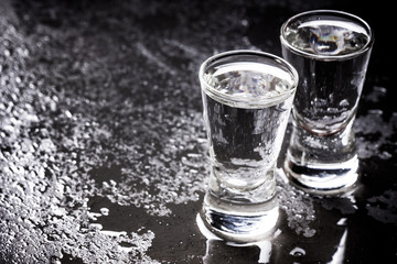 Vodka shots on wet black surface.