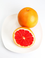 Ripe grapefruit with half on a plate over  white background clos