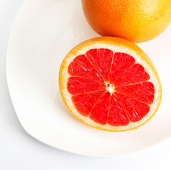 Ripe grapefruit with half on a plate over  white background clos