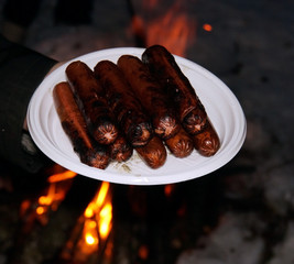 Smoked sausages on white plastic plate on the background of fire