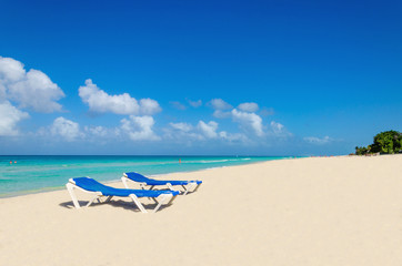 Blue sunbeds on sandy Caribbean beach against blue sky