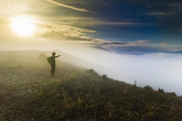 man standing on a hill in foggy weather at sunset