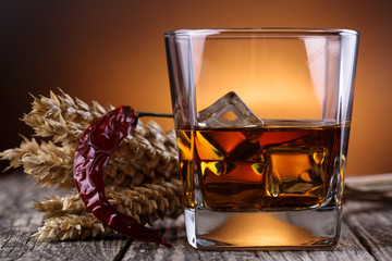 Glass of whiskey with ice and wheat on a wooden table.