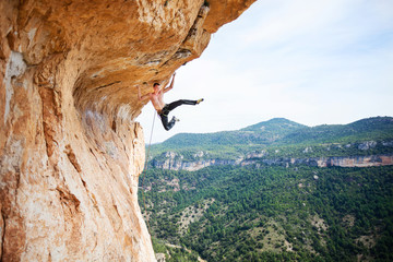 Young man climbing up ledge of cliff