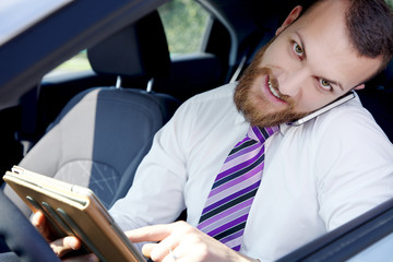 Smiling cool young business man at work in car with technology