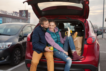 Happy couple sitting at car trunk after shopping