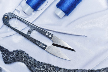 Scissors and blue thread on fabric background.