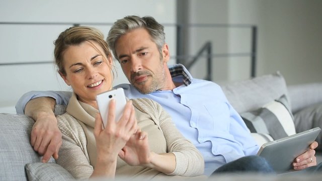 Mature couple at home using tablet and smartphone