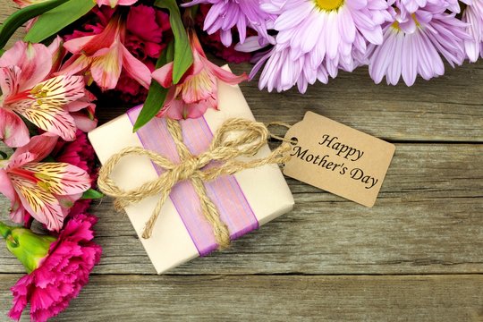 Flowers with gift box and Mother's Day tag on wood background