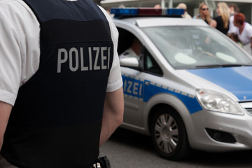 Polizist und Streifenwagen vor einer Menschenmenge