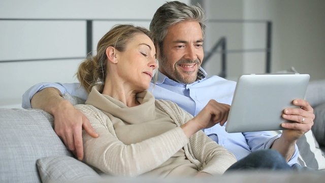 Mature couple relaxing in sofa and using digital tablet